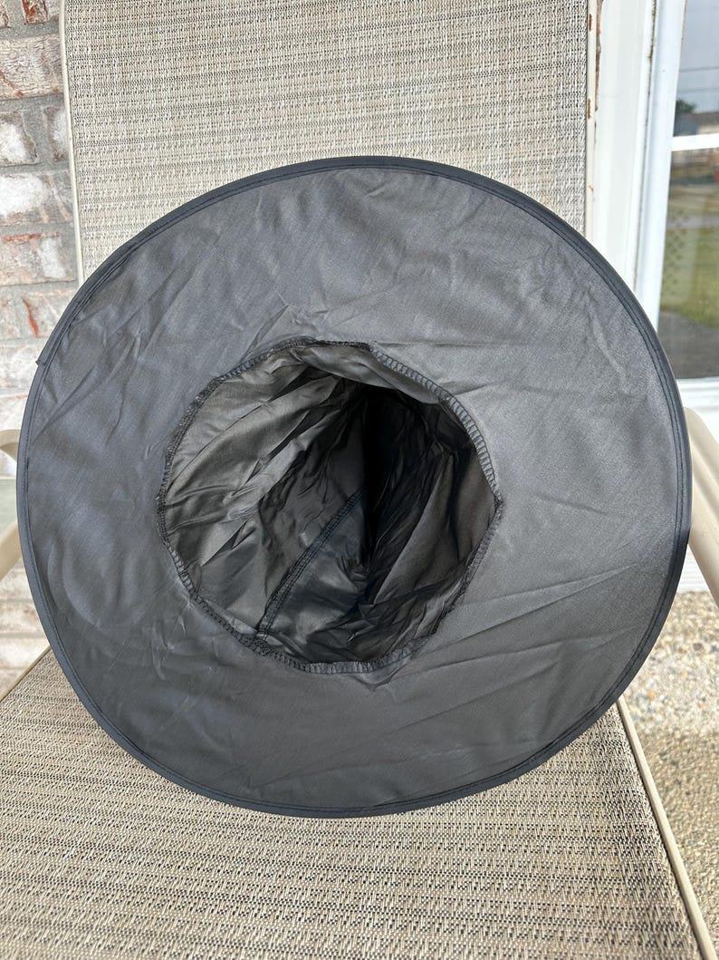 May include: A black pointed hat with a wide, circular brim and a tall, conical crown. The hat is constructed from a smooth, dark fabric with visible stitching along the inner rim and the base of the crown, creating a structured, hollow shape.
