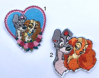 Puede incluir: Dos parches bordados con Lady y la Tramp. El primer parche muestra a Lady y la Tramp en un marco en forma de corazón con flores rosas. El segundo parche muestra a Lady y la Tramp abrazándose.
