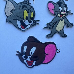 May include: Three embroidered patches featuring cartoon characters. One patch depicts a gray cat with yellow eyes and a white mouth. Another shows a gray mouse with pink ears and a tan belly. The third patch is a brown mouse with a pink ear.