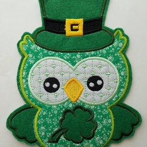 May include: Green felt owl wearing a green felt leprechaun hat with a gold buckle. The owl is holding a green shamrock.