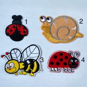 Op de afbeelding: Vier geborduurde strijkpatches met een lieveheersbeestje, een slak, een bij en een lieveheersbeestje. De patches zijn genummerd van 1 tot en met 4.