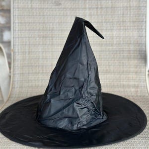 May include: A black pointed hat with a wide, circular brim. The hat is constructed from a lightweight, slightly wrinkled fabric material that forms a tall, conical crown that bends slightly at the very top point of the structure.
