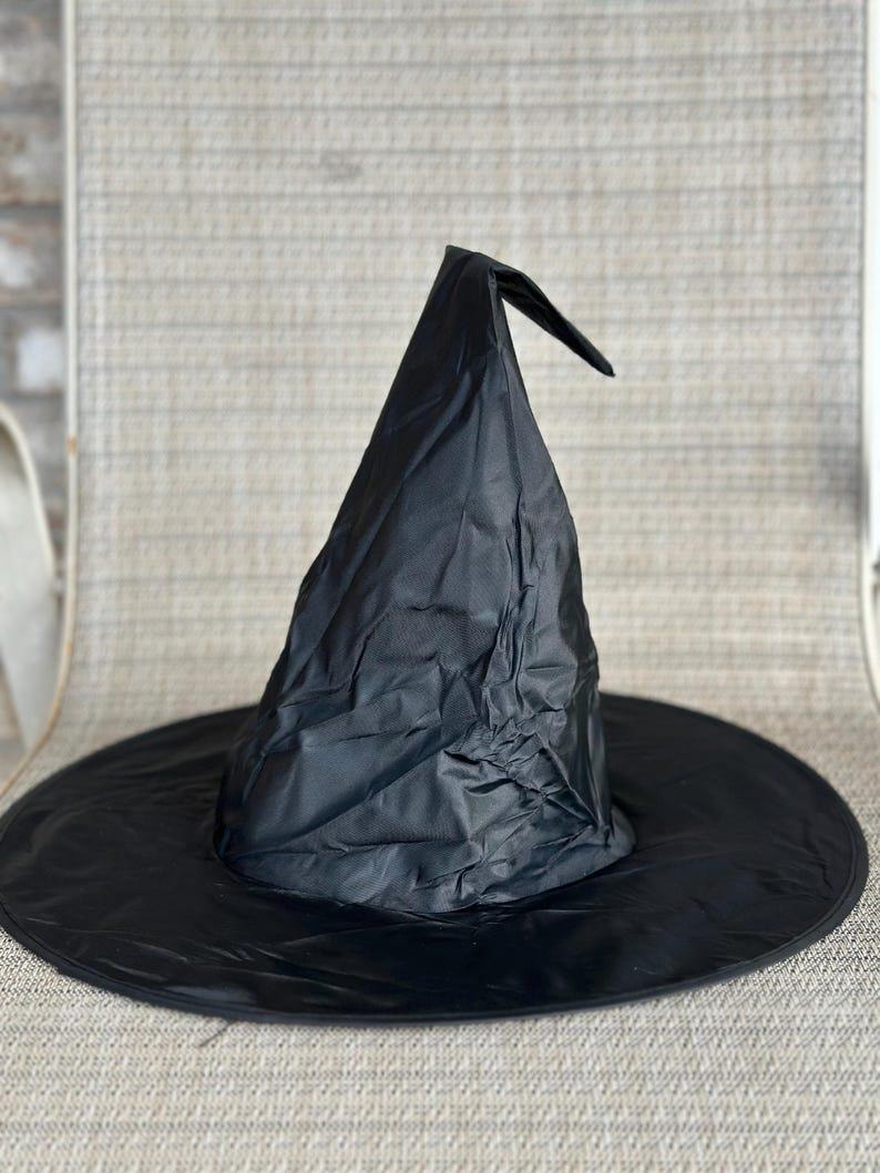 May include: A black pointed hat with a wide, circular brim. The hat is constructed from a lightweight, slightly wrinkled fabric material that forms a tall, conical crown that bends slightly at the very top point of the structure.