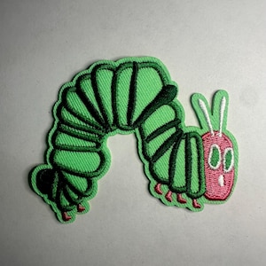 May include: Embroidered patch featuring a green caterpillar with a red face and small red feet. The caterpillar has black stripes and white antennae. The patch is designed with a cartoon style and is likely for clothing or accessories.