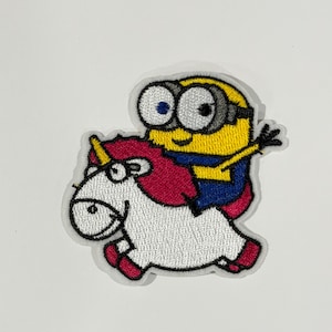 Pode incluir: Um emblema bordado apresentando um personagem Minion amarelo com óculos grandes montado num unicórnio branco com crina rosa e chifre amarelo. O Minion veste jardineiras azuis e tem um braço levantado. O emblema tem uma borda branca e detalhes costurados.