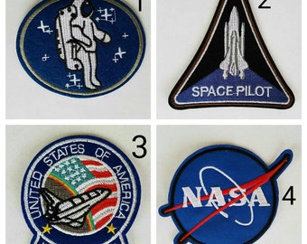 Può includere: Quattro toppe ricamate con disegni a tema spaziale. Una toppa presenta un astronauta, un'altra recita "SPACE PILOT" con uno shuttle, una terza mostra la bandiera americana e le parole "UNITED STATES OF AMERICA ASTRONAUT", e l'ultima ha il logo della NASA.