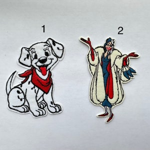 May include: Two embroidered iron-on patches. The first patch is a white Dalmatian puppy with red spots and a red bandana. The second patch is Cruella De Vil from Disney's 101 Dalmatians. She is wearing a white fur coat with red accents and a blue dress.