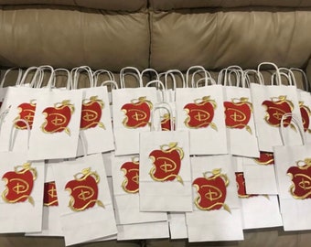 Pode incluir: Uma pilha de sacos de presente de papel branco com desenhos de maçãs vermelhas e logotipos Disney dourados.