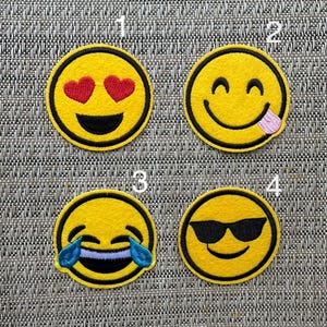 May include: Four yellow embroidered iron-on patches with different smiley faces. The first patch has hearts for eyes, the second has a tongue sticking out, the third has tears of joy, and the fourth has sunglasses.