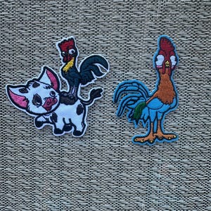 May include: Two embroidered patches featuring characters from the animated film Moana. One patch shows a white pig with black spots riding a black rooster with a red comb. The other patch shows a blue rooster with a red comb and a green tail.