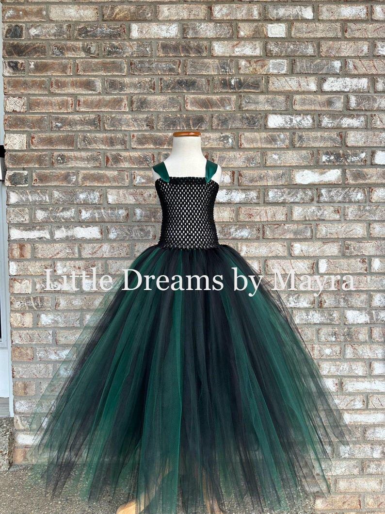 May include: A floor-length dress featuring a black crocheted bodice with dark green shoulder straps and a voluminous skirt made of layered black and dark green tulle. The text Little Dreams by Mayra is overlaid across the center of the image.