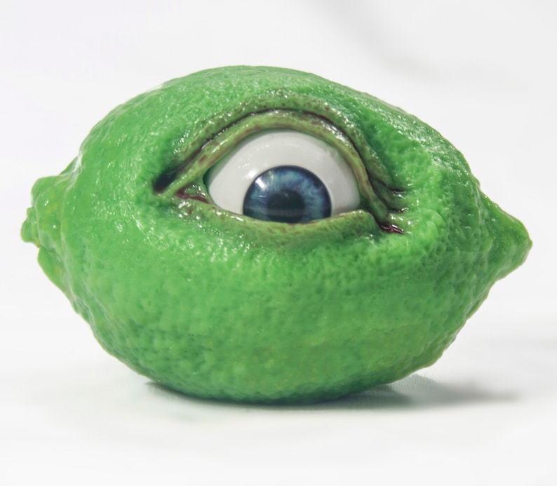 May include: A green lime with a realistic blue eye painted on it.