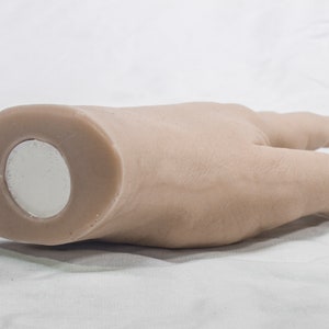 May include: A light brown hand-shaped object with a round, silver magnet on the bottom.