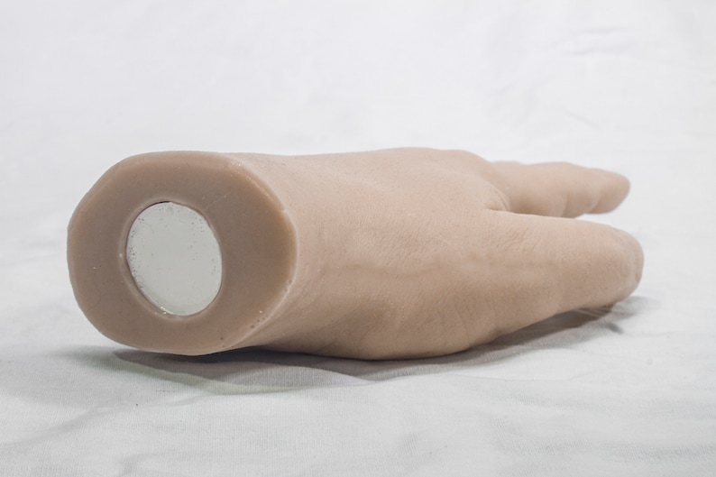 May include: A light brown hand-shaped object with a round, silver magnet on the bottom.