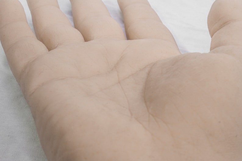 May include: A close-up of a light-skinned hand with visible lines and wrinkles. The hand is resting on a white surface.