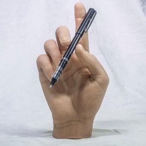 May include: A black pen with a silver clip and clear ink chamber is held in a hand. The pen is positioned at an angle, suggesting it is ready to write. The background is a plain white surface.