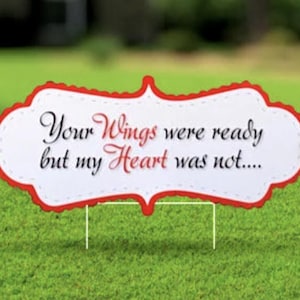 May include: A white sign with red trim and scalloped edges reads "Your Wings were ready but my Heart was not..."  The sign is on a green lawn with red hearts and flowers.