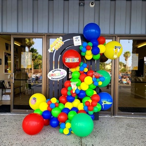 Pu&ograve; includere: Un arco di palloncini colorati decorato con le parole "Curious Caterpillars" e "Woo Hoo!" L'arco &egrave; fatto di palloncini rossi, gialli, blu e verdi. Ci sono anche alcuni piccoli palloncini bianchi con punti neri.