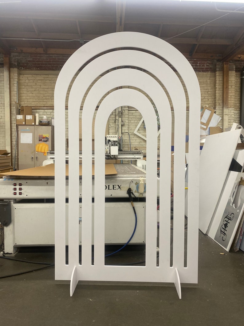 Pu&ograve; includere: Arco in legno bianco con tre archi concentrici ritagliati. L'arco &egrave; in piedi su un pavimento bianco in un laboratorio.