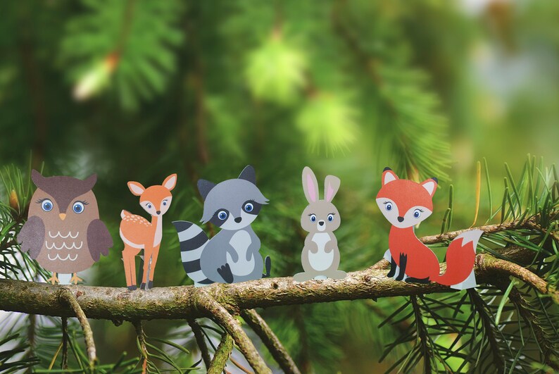 May include: Five paper cutouts of woodland animals on a pine branch. The animals are an owl, a deer, a raccoon, a rabbit, and a fox. The animals are all facing forward and are arranged in a line.