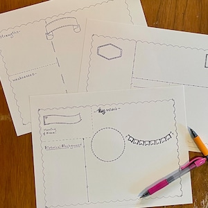 May include: Several white paper sheets with hand-drawn templates for journaling or note-taking. The templates include banners, circles, and lines. Two pens, one orange and one pink, are also visible, along with a roll of decorative tape.