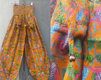 Broek in haremstijl. Wijde pijpen met gesmokte taille en elastische enkel. Bloemenprint op mosterdachtergrond