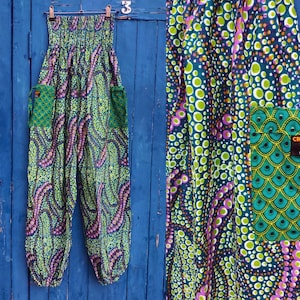May include: A pair of patterned harem pants with a green, purple, and white dot design. The pants have two green pockets with a scale-like pattern. The waistband is elasticized. The pants are hanging on a clothesline against a blue wooden background.