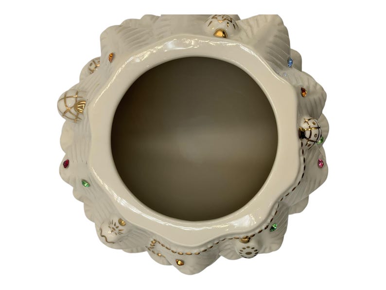 May include: A white ceramic Christmas tree cookie jar with gold trim and colorful jewels. The jar is open and the inside is visible.