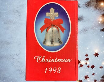 May include: A red box with a silver bell ornament with a red bow and a cross on top. The box says "Christmas 1998" on the front.