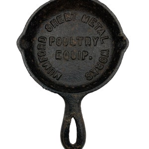 Puede incluir: Sart&eacute;n de hierro fundido negro con mango. La sart&eacute;n tiene las palabras "Mulford Sheet Metal Works Poultry Equip." grabadas en relieve.