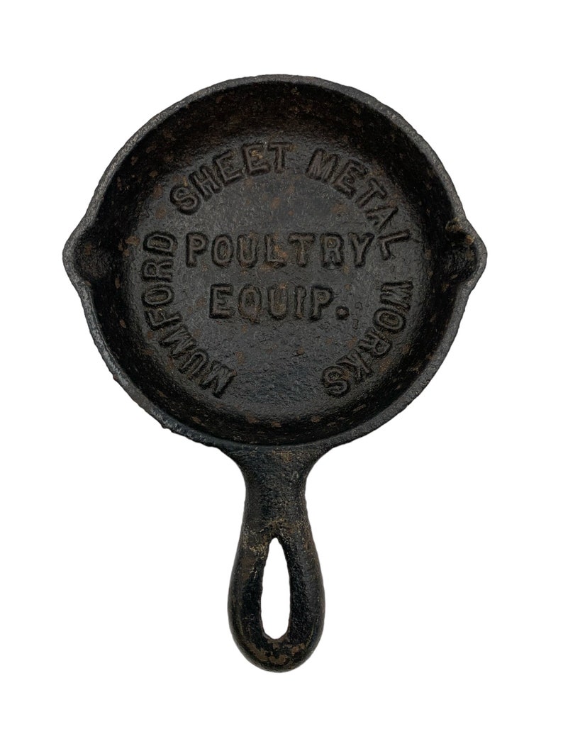 Puede incluir: Sart&eacute;n de hierro fundido negro con mango. La sart&eacute;n tiene las palabras "Mulford Sheet Metal Works Poultry Equip." grabadas en relieve.