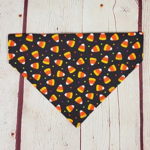 K&ouml;nnte beinhalten: Schwarzes dreieckiges Haustier-Bandana mit einem sich wiederholenden Muster aus Candy Corn und kleinen bunten Punkten. Das Candy Corn ist orange, gelb und wei&szlig;. Das Bandana ist aus Stoff und f&uuml;r Halloween geeignet.