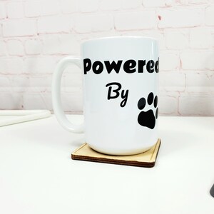 May include: White ceramic coffee mug with a black paw print and the text "Powered By" on a wooden coaster.
