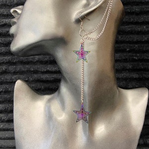 May include: A silver ear cuff with a chain attached to a silver earring with two iridescent star charms. The stars have a rainbow effect with a purple hue.