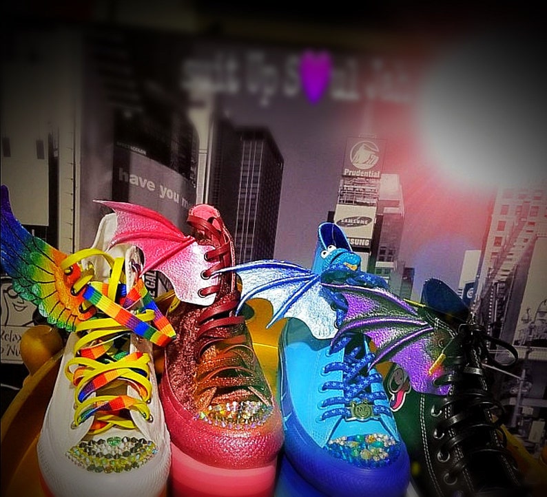 May include: Four pairs of high-top sneakers with colorful wings and laces. The sneakers are pink, blue, white, and black. The wings are made of fabric and are attached to the shoes with velcro. The laces are rainbow, purple, yellow, and black.