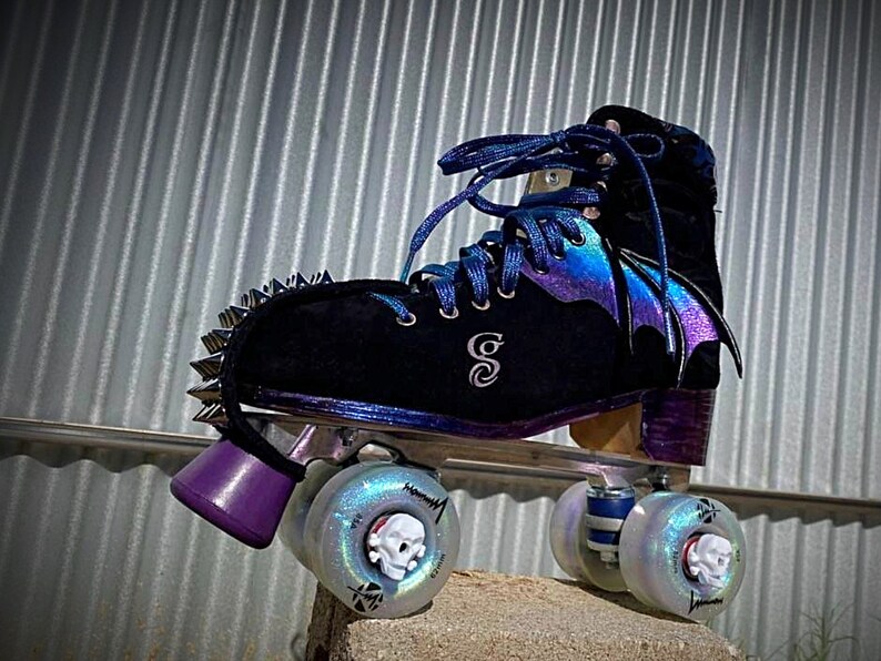 May include: Black roller skates with iridescent purple and blue wings, silver studs, and skull-shaped wheels.