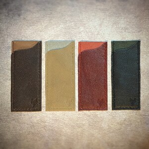 May include: Four leather card holders in different colors: brown, beige, red, and black. Each holder has a stitched edge and a textured surface.