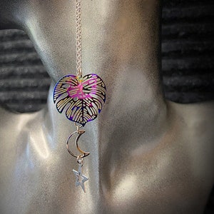 May include: A gold necklace with a iridescent purple and blue leaf pendant, a crescent moon charm, and a star charm.