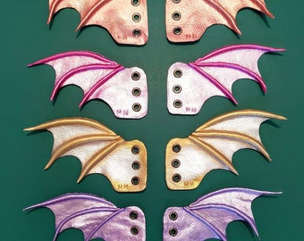 May include: Six pairs of leather dragon wing-shaped keychains in pink, gold, purple, and peach. Each keychain has a small metal loop for attaching keys.
