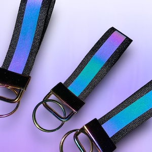 May include: Three black keychains with iridescent blue and purple stripes. Each keychain has a silver metal ring.