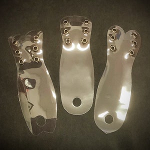 Könnte beinhalten: Drei transparente Schuheinlagen aus Kunststoff mit Metallösen. Die Einlagen sind fußförmig und haben ein Loch am Boden.