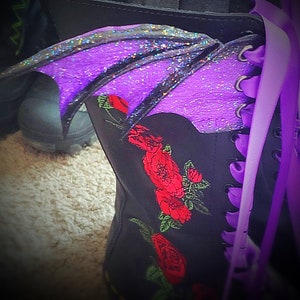 May include: A black boot with purple glitter wings and red embroidered roses. The boot has purple laces.