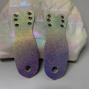 May include: Two iridescent purple and green leather straps with multiple silver eyelets. The straps are shaped like a teardrop with a rounded top and a pointed bottom.