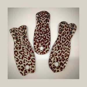 Può includere: Tre toppe in pelle con stampa leopardata marrone e bianca con occhielli metallici. Le toppe hanno la forma di una lacrima, un rettangolo e un cuore.