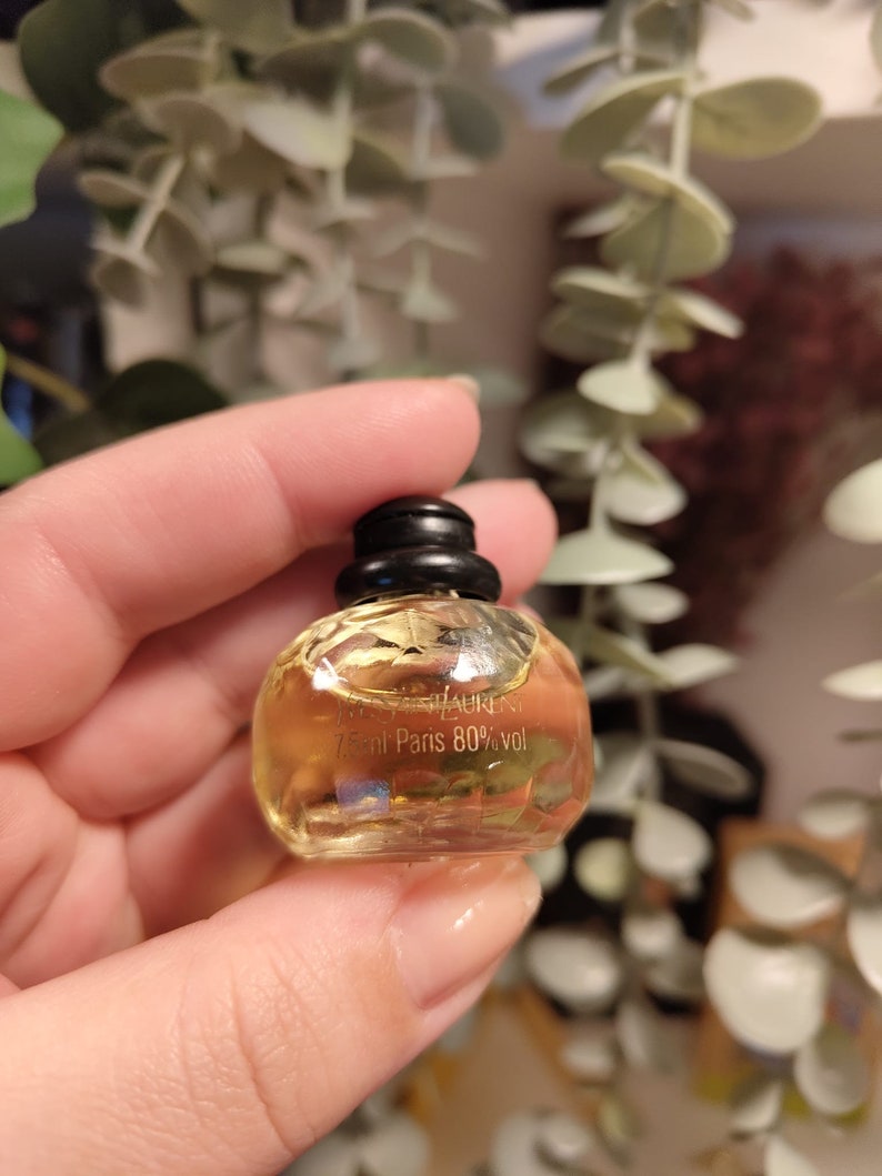 Puede incluir: Un peque&ntilde;o frasco de perfume de vidrio transparente con una tapa negra. El frasco est&aacute; etiquetado con "Yves Saint Laurent 7,5 ml Paris 80% vol."