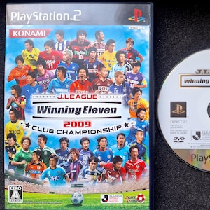 May include: A PlayStation 2 game case and disc for J.League Winning Eleven 2009 Club Championship. The case features a group of football players in blue and white kits. The disc has a silver background with the text "J.League winning Eleven Tactics."
