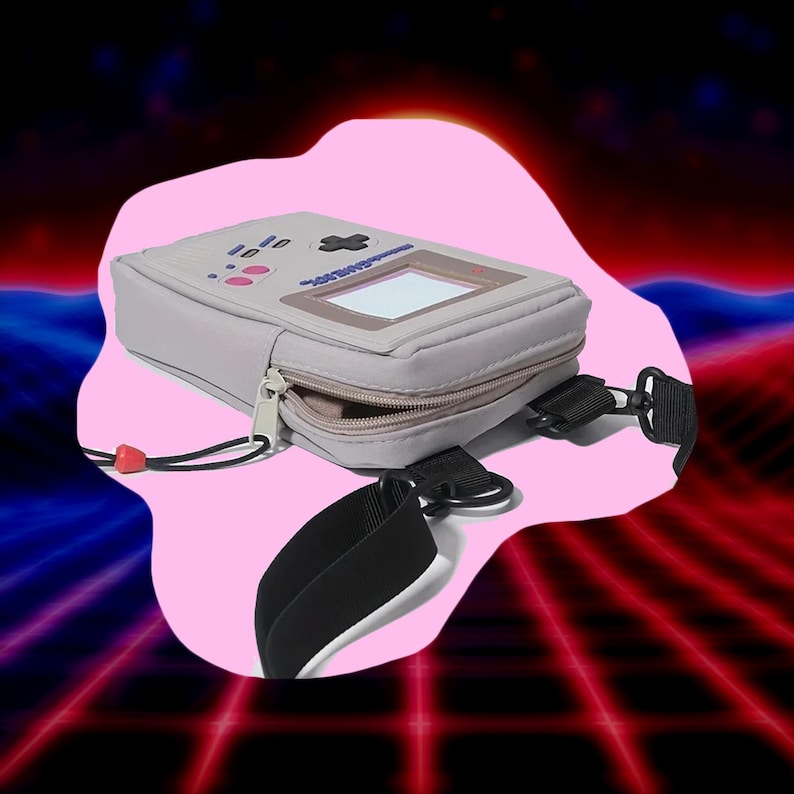 May include: A light gray crossbody bag designed to resemble a retro handheld gaming device. The bag features a zipper closure, a clear screen, and a black strap. Pink and blue accents are visible on the bag's surface.