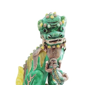May include: A green and yellow ceramic foo dog statue with a smaller foo dog in its paw. The statue is standing on a square base with floral and butterfly designs.