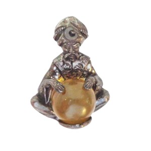 May include: A silver figurine of a person wearing a turban and holding a yellow crystal ball.
