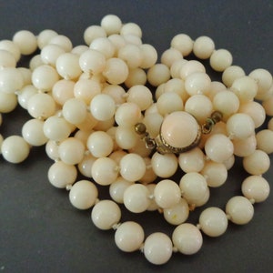 May include: A long strand of pale pink coral beads with a gold clasp. The beads are round and smooth.